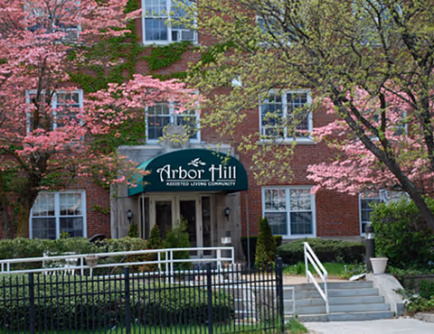 Front view of Arbor Hill Assisted Living building with pink blossoming trees.