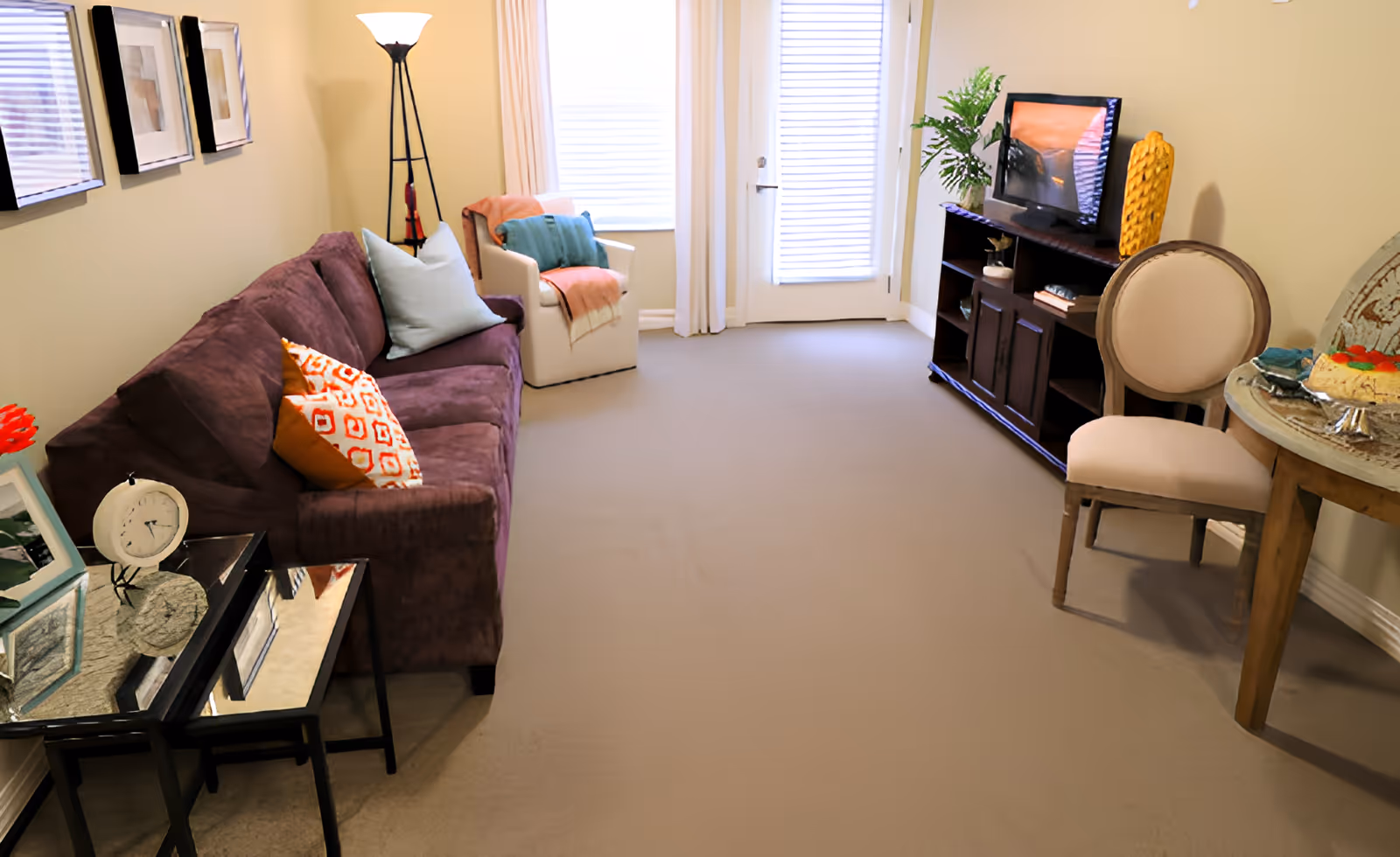 Bright furnished living room with a purple sofa, armchair, TV on a stand and a small round table.