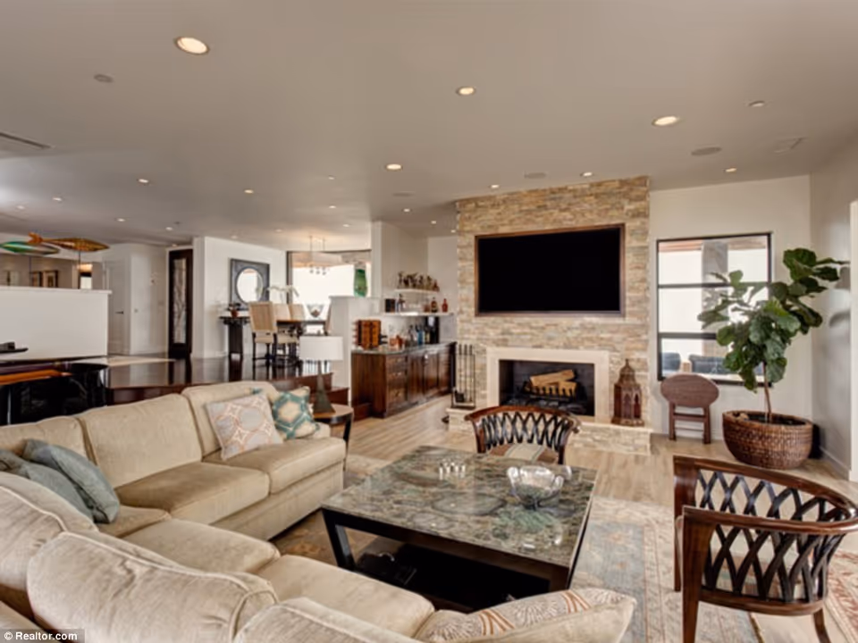 Spacious modern living room with a sectional sofa, stone fireplace with mounted TV, coffee table and open dining area.