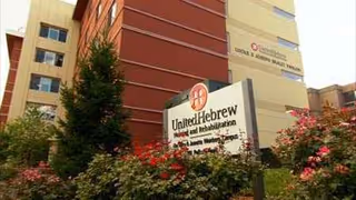 Exterior view of United Hebrew of New Rochelle building with sign and shrubs.