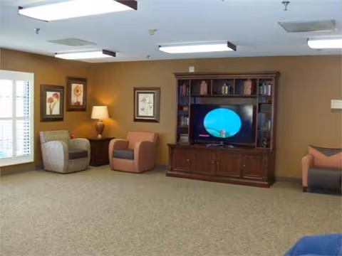 A senior living lounge with a large TV, seating area, and warm framed art.