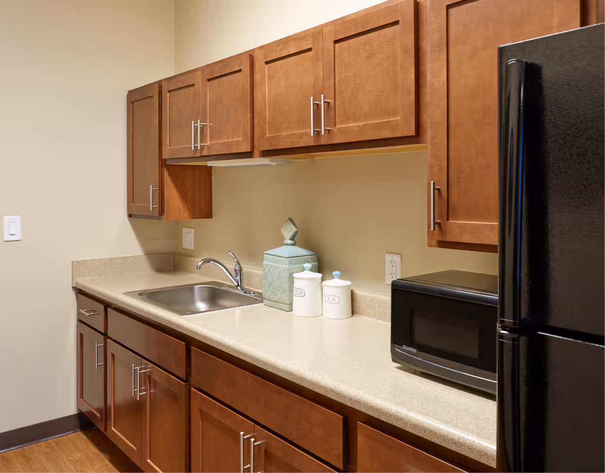 Small kitchen countertop with sink, wooden cabinets, a microwave, and a refrigerator.