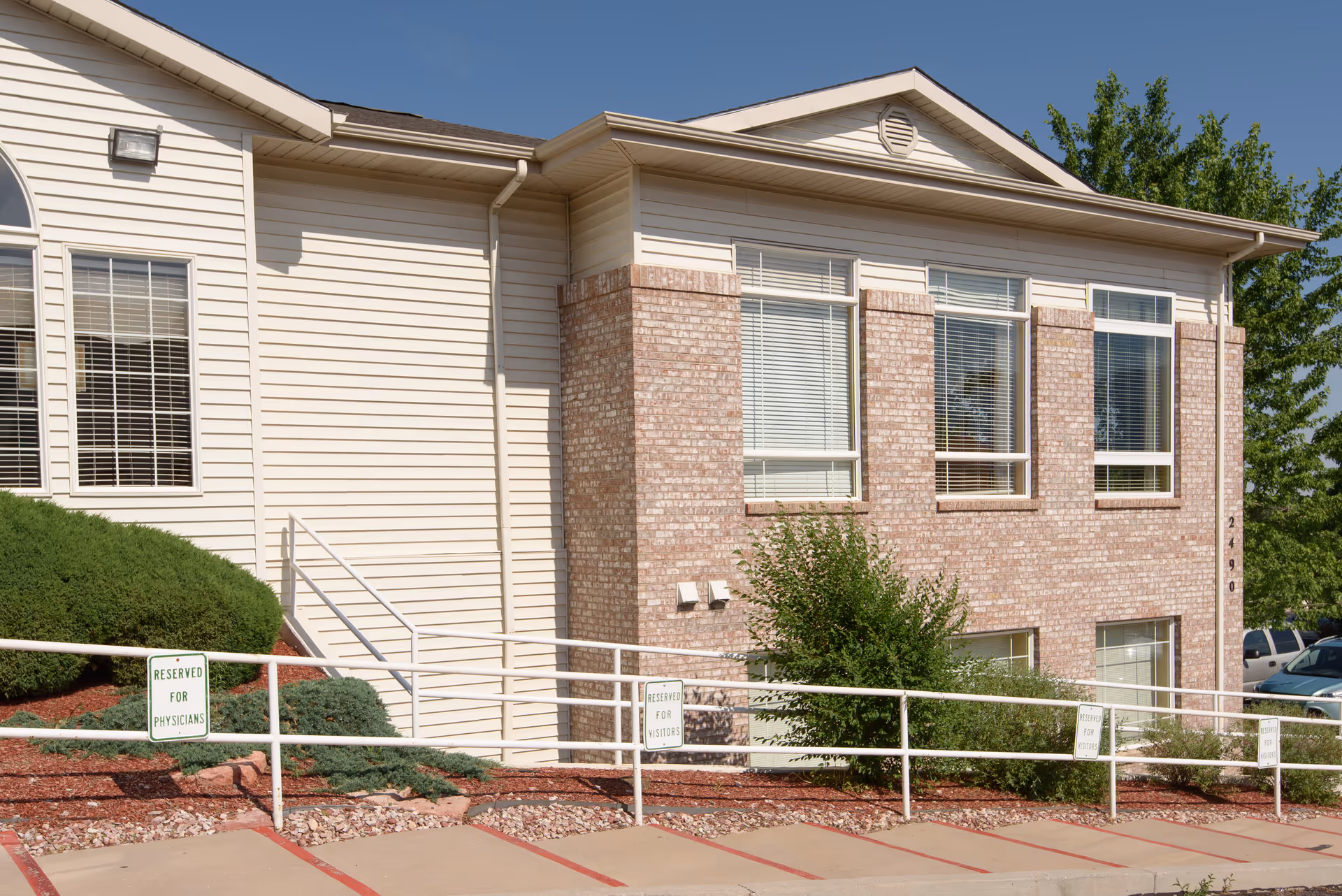 Exterior front of a light-colored two-story brick and siding building with large windows, a railing ramp, and reserved parking signs.