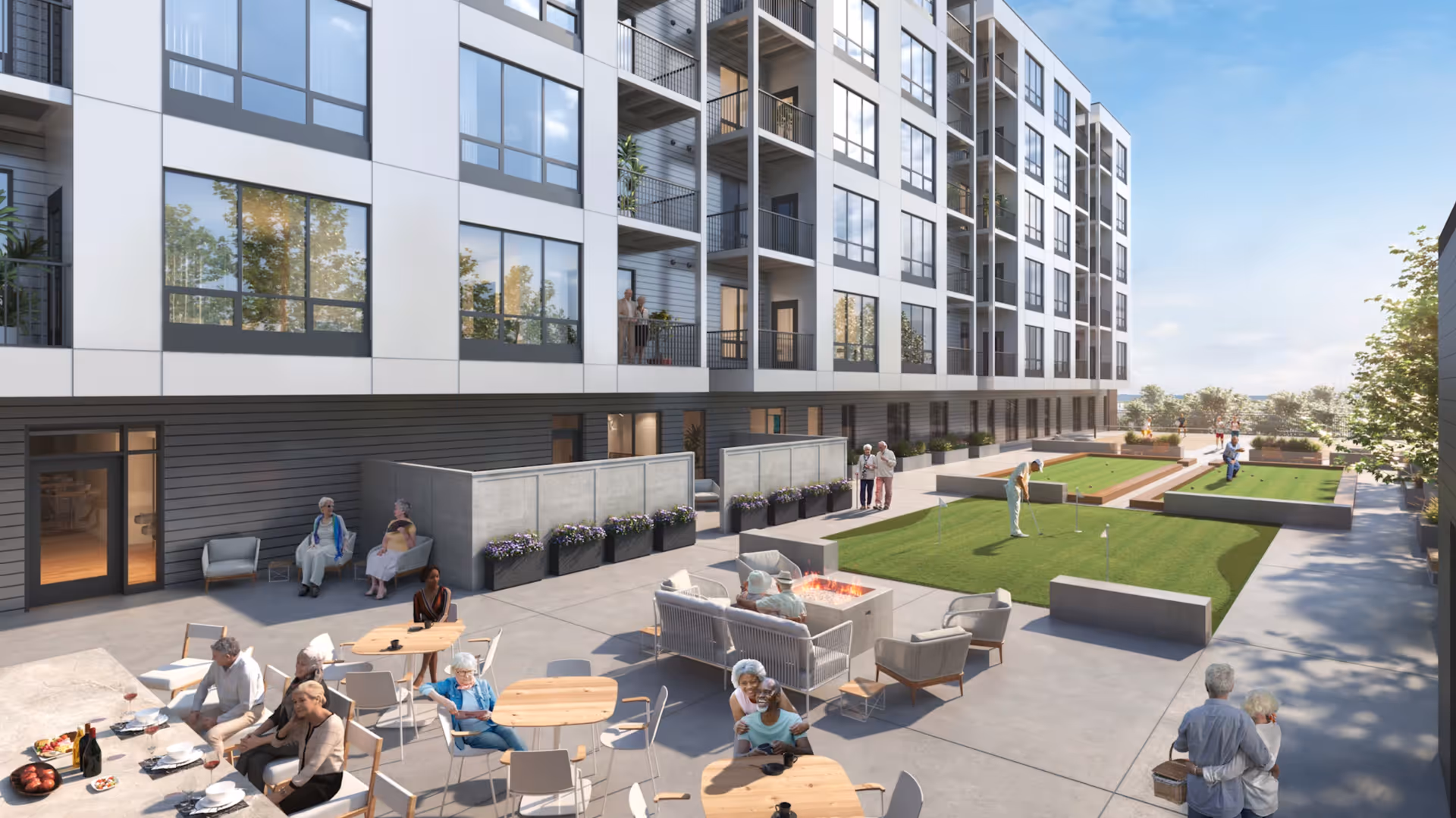 Outdoor patio area of a senior living facility with several elderly people sitting at tables, socializing, and relaxing near a fire pit. Some residents are playing lawn games on the grass, while others stand on balconies of the multi-story building overlooking the courtyard. The scene is bright and sunny with clear skies.