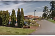 Exterior view of Pioneer Place senior living facility with a driveway, trees, and red-roofed building.