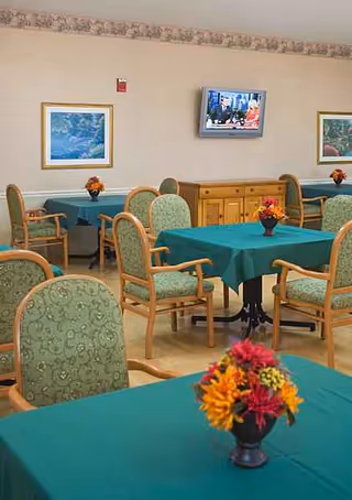 Dining room with teal tablecloths, floral centerpieces, and green upholstered chairs.