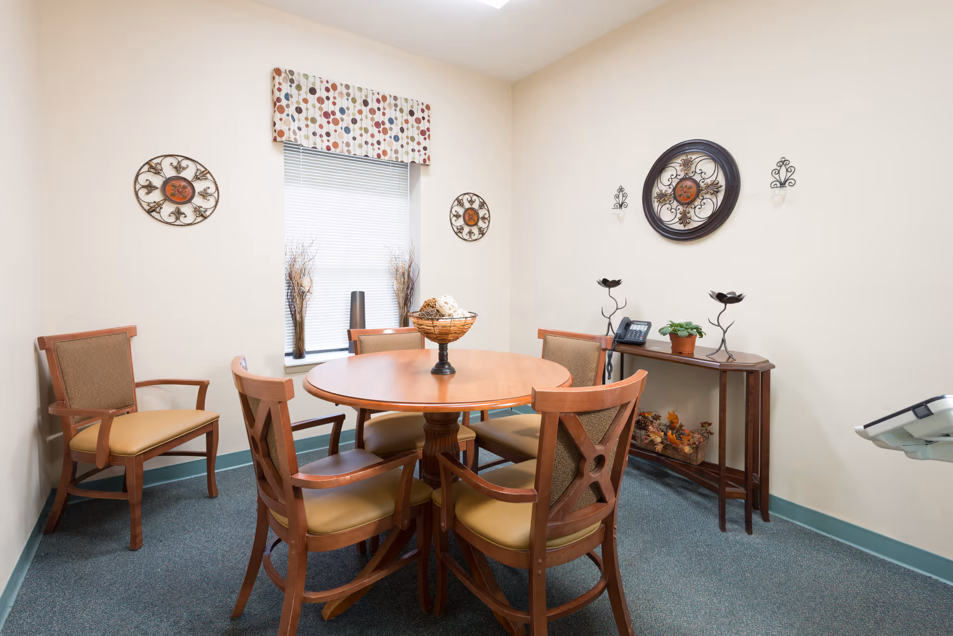 Small communal dining room with a round wooden table surrounded by chairs, a side console table, and decorative wall art.