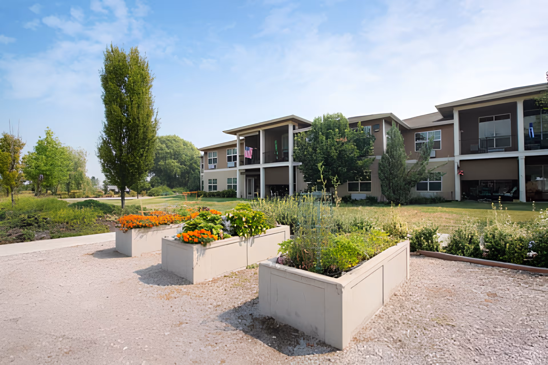 Exterior view of a two-story senior living building with raised flower planters and landscaped grounds.