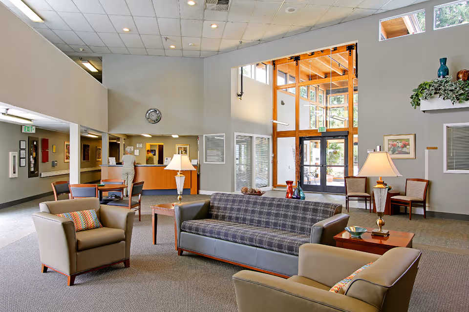 Bright common area with sofas and armchairs, a reception desk, and a large glass entrance.