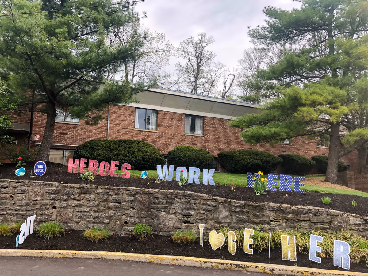 Brick facility front with landscaped beds and lawn signs reading 'HEROES WORK HERE' and decorative letters spelling 'TOGETHER'.