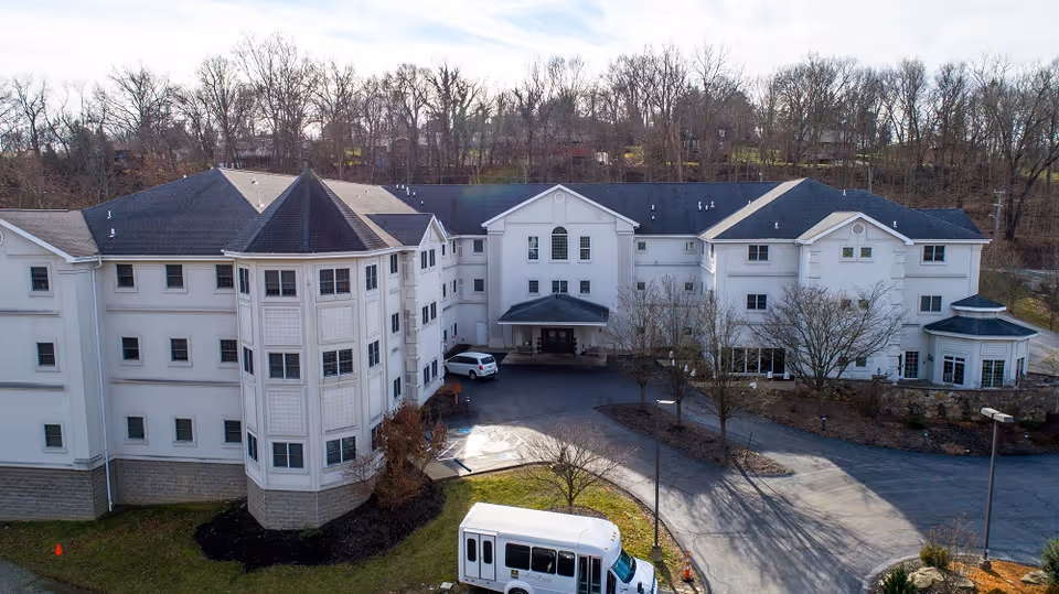 Aerial view of a white multi-wing senior living facility with a front entrance and bus.