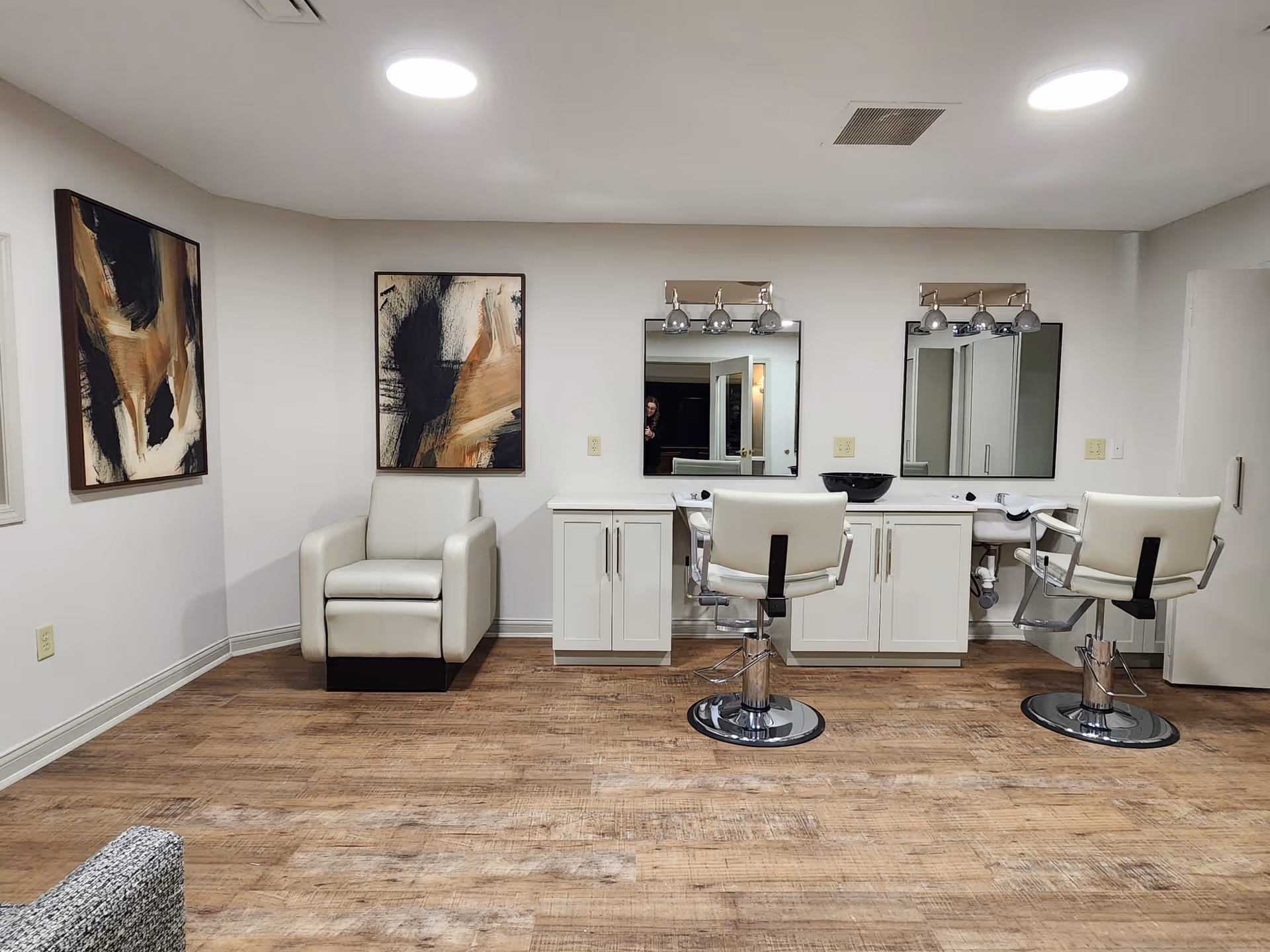 A modern salon interior featuring two styling chairs, mirrors, and abstract art on the walls, with wooden flooring.