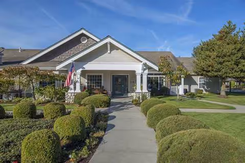 Front exterior of a single-story senior living facility with manicured hedges and flag