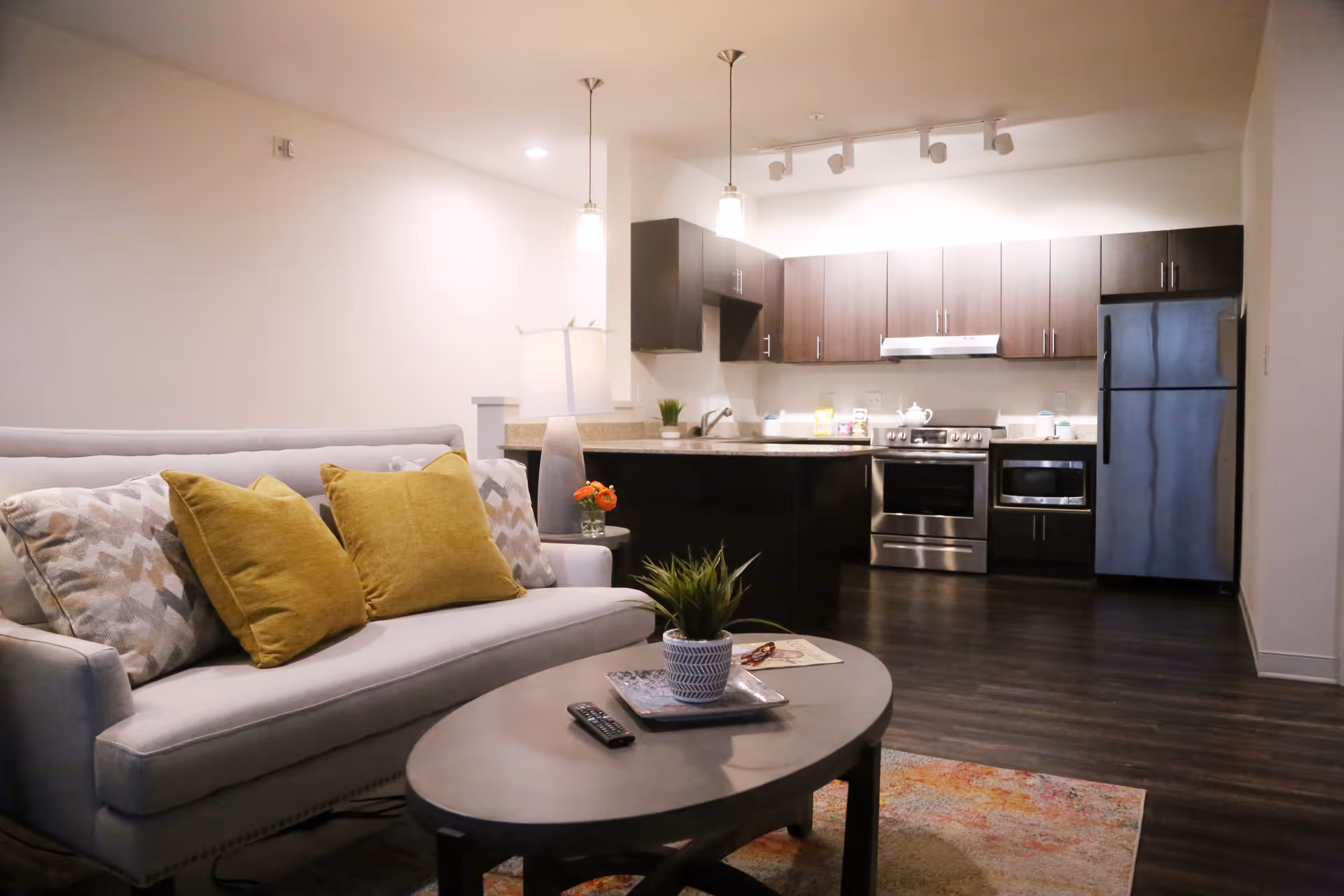 Open-plan living area with a sofa and coffee table in front of a modern kitchen with an island and stainless steel appliances.