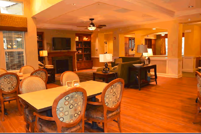 Warm communal dining and lounge area with tables and patterned chairs in the foreground and a seating area with lamps and a fireplace in the background.