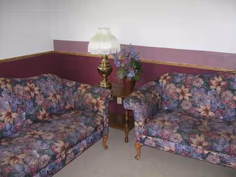 Two floral upholstered sofas face a small side table and lamp in a living room.