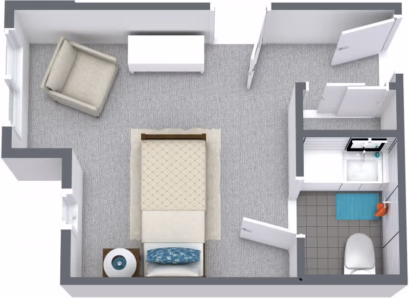 Top-down view of a small apartment floor plan showing a bedroom with a bed, armchair, nightstand with a lamp, and a dresser. Adjacent to the bedroom is a bathroom with a toilet, sink, and shower area.
