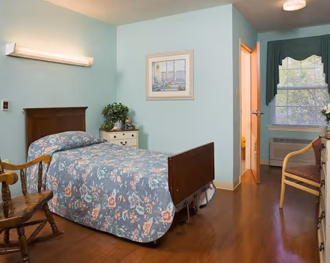 Pastel blue bedroom in senior facility with floral quilted bed and furniture.