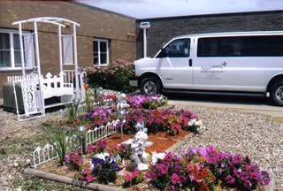 White van parked beside a brick building with a colorful garden in foreground.