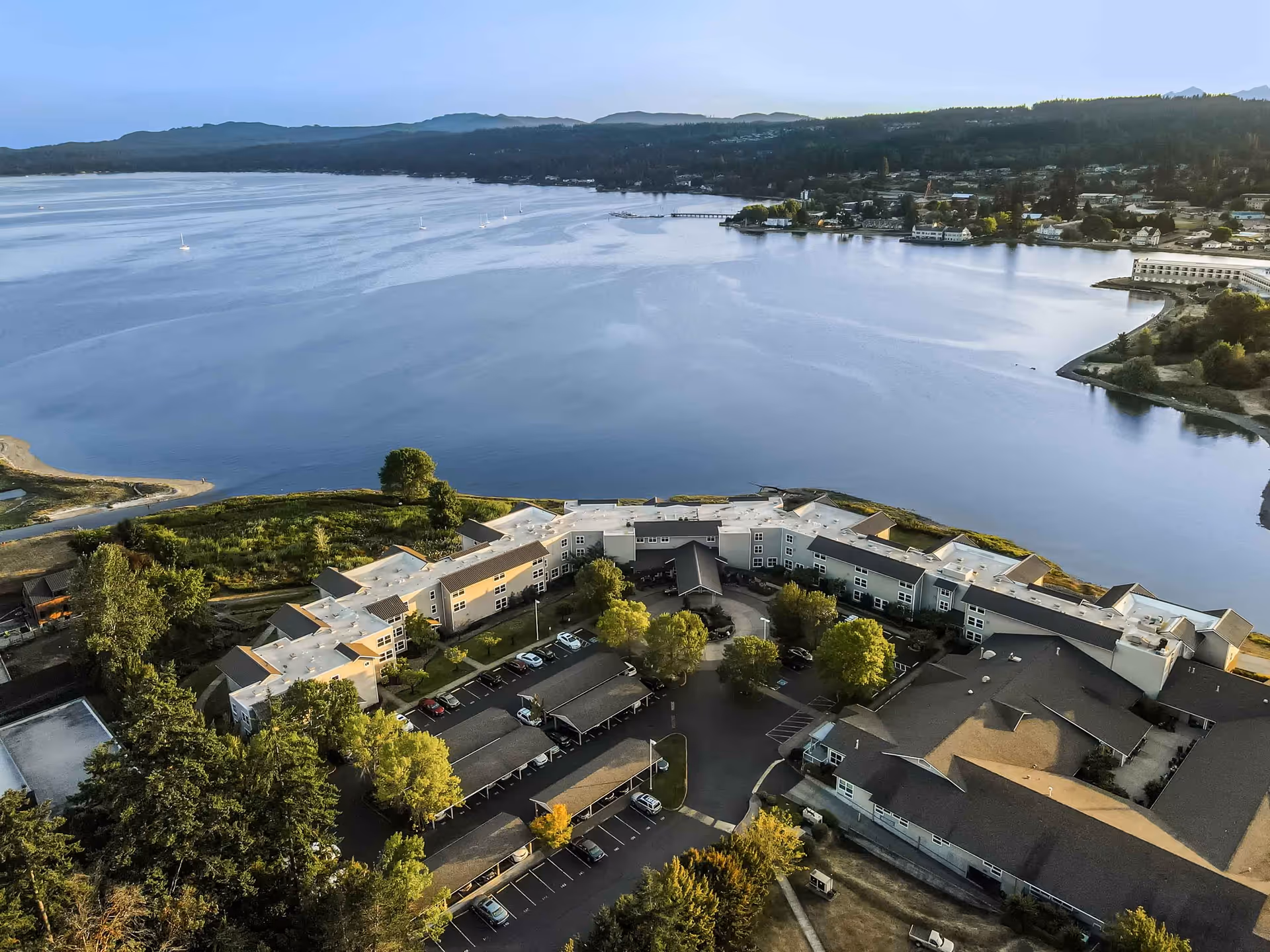 Aerial view of a senior living facility named Crista Shores located next to a large body of water with surrounding greenery and parking areas.
