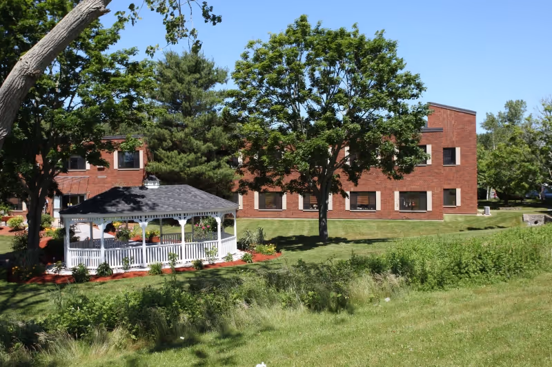 Brick rehabilitation building with a white gazebo on a grassy lawn and trees under a clear blue sky.