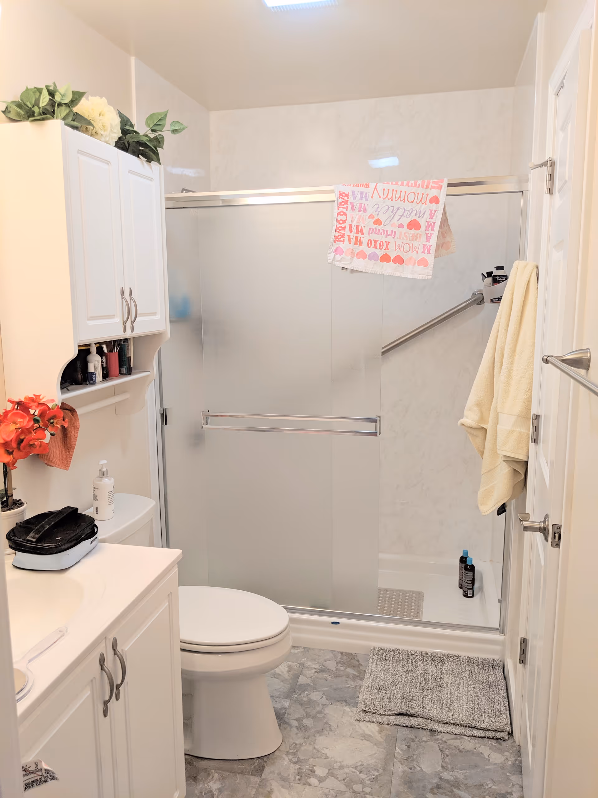 Small bright bathroom featuring a vanity and toilet on the left and a frosted glass sliding-door shower with towels on the right.