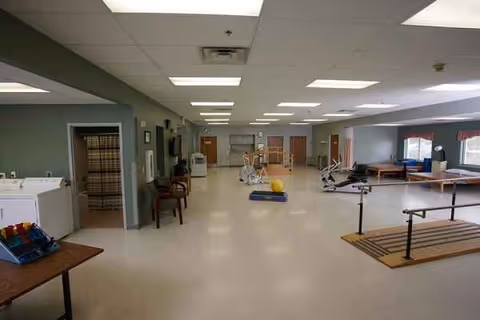 Wide interior gym area in a Willows Nursing and Rehab facility with exercise equipment and mats.