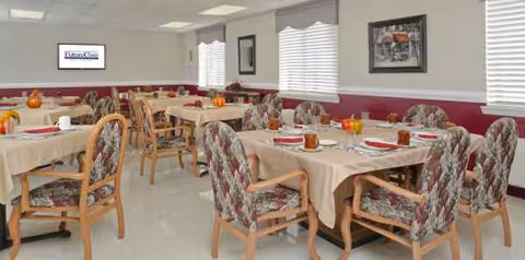 Bright dining room with beige tablecloths, patterned chairs, and pumpkins on tables.