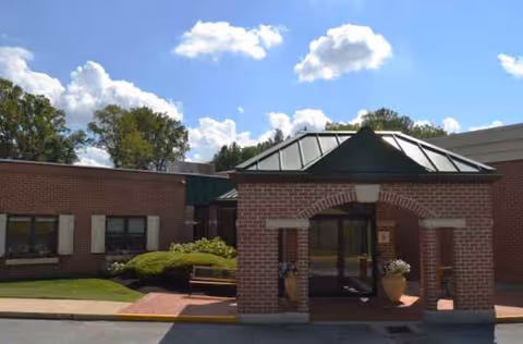 Exterior brick building entrance with glass doors and a green metal roof canopy.