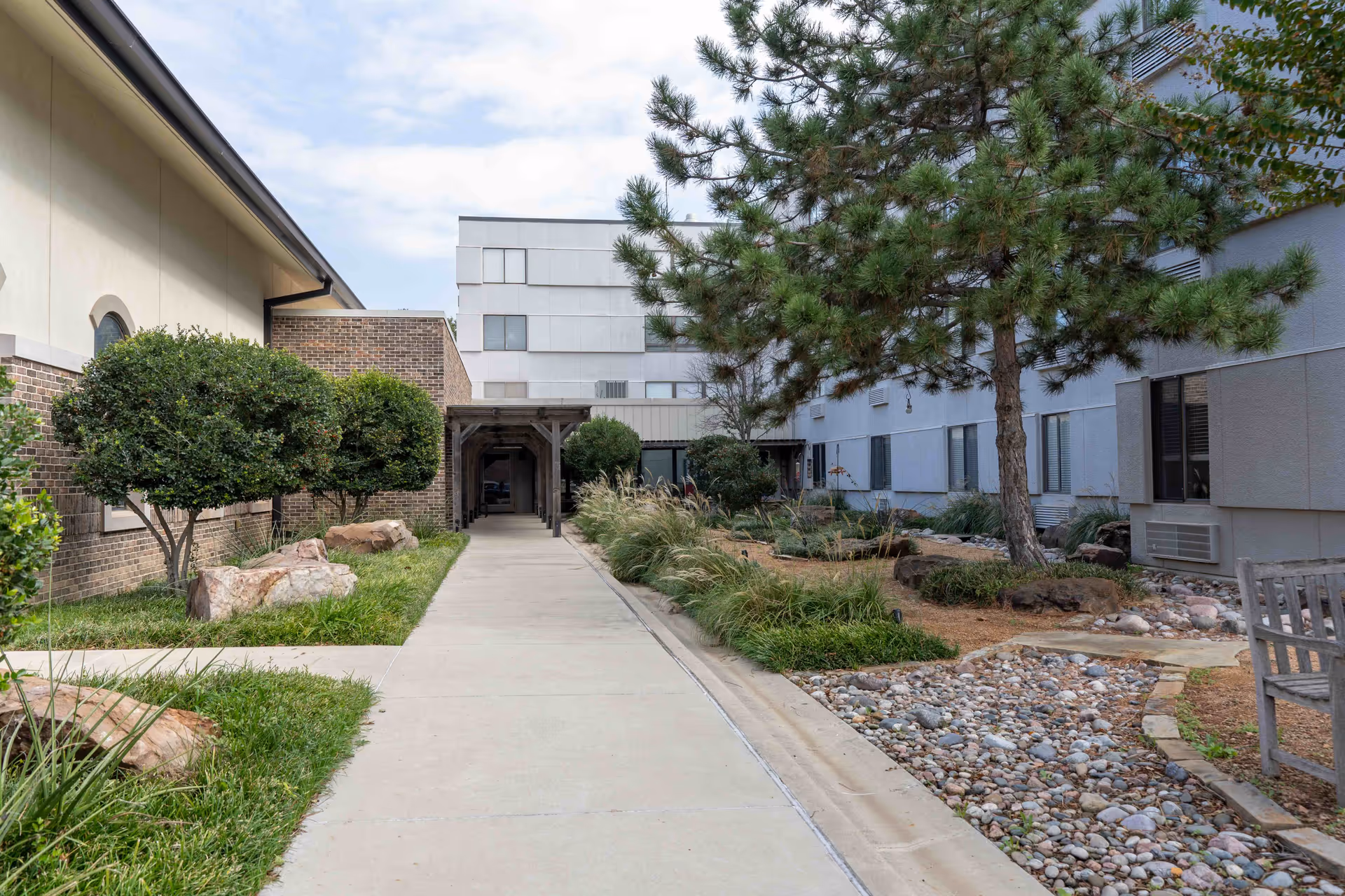 A paved walkway through a landscaped courtyard between Morrison Residence buildings with trees, rocks, and benches.
