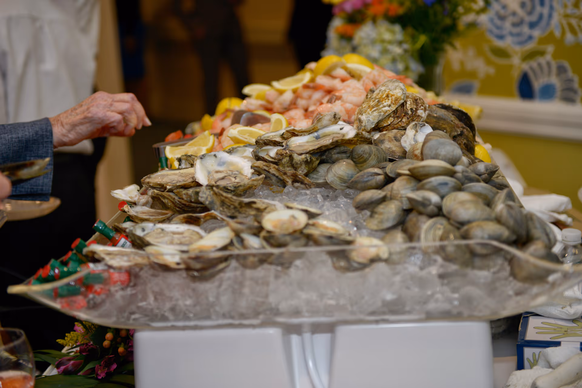 Tray of oysters, clams and shrimp on ice with lemon wedges at a buffet table.