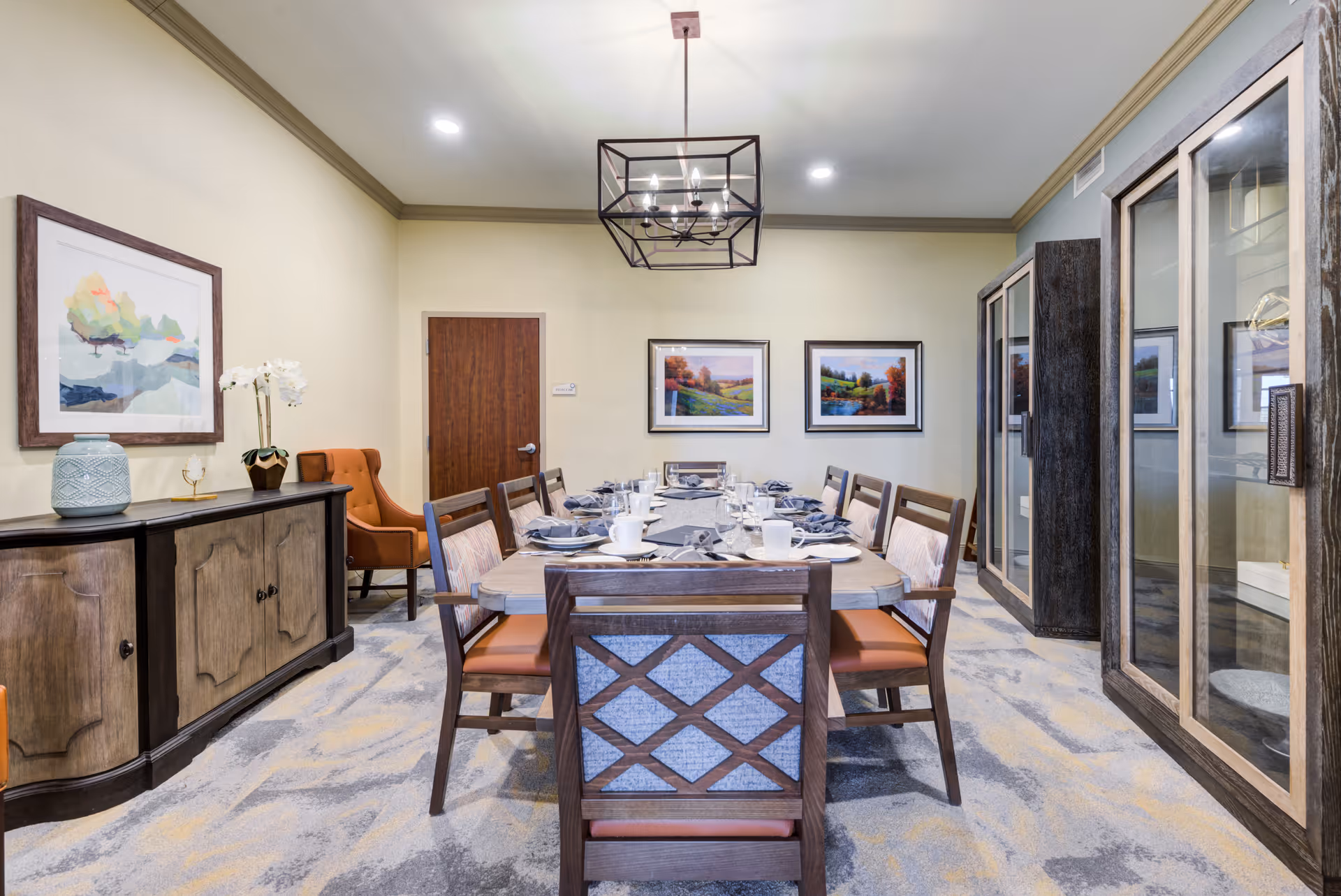 Dining room with a long set table, wooden chairs, sideboard, framed artwork, and an overhead chandelier.