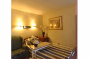 Small sitting area with a couch, coffee table holding a floral arrangement, striped rug, wall sconces, and framed artwork.