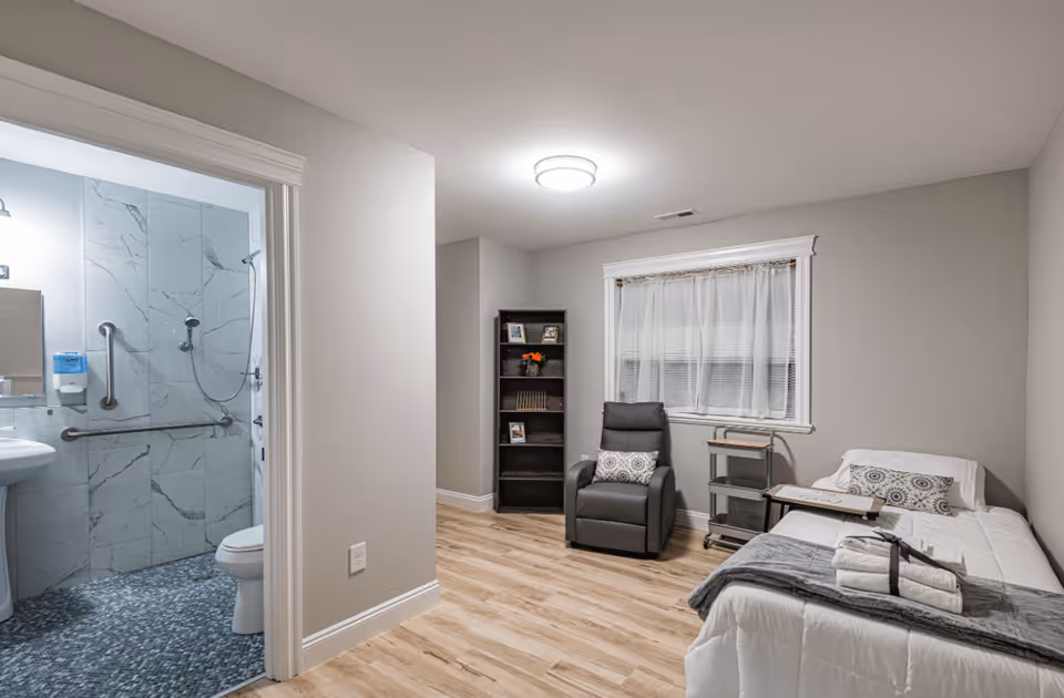Private bedroom with a single bed, recliner, bookshelf and an open door showing an accessible bathroom.