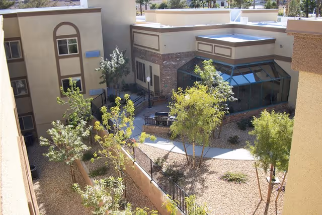 An outdoor courtyard at a senior living facility with trees, walkways, and a glass entrance.