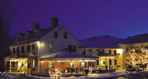 Night exterior of The Lincoln Home Senior Retirement Community with warm lights and snow-covered surroundings.