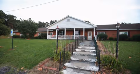 Front exterior of a brick senior living facility with a white porch and stairs.