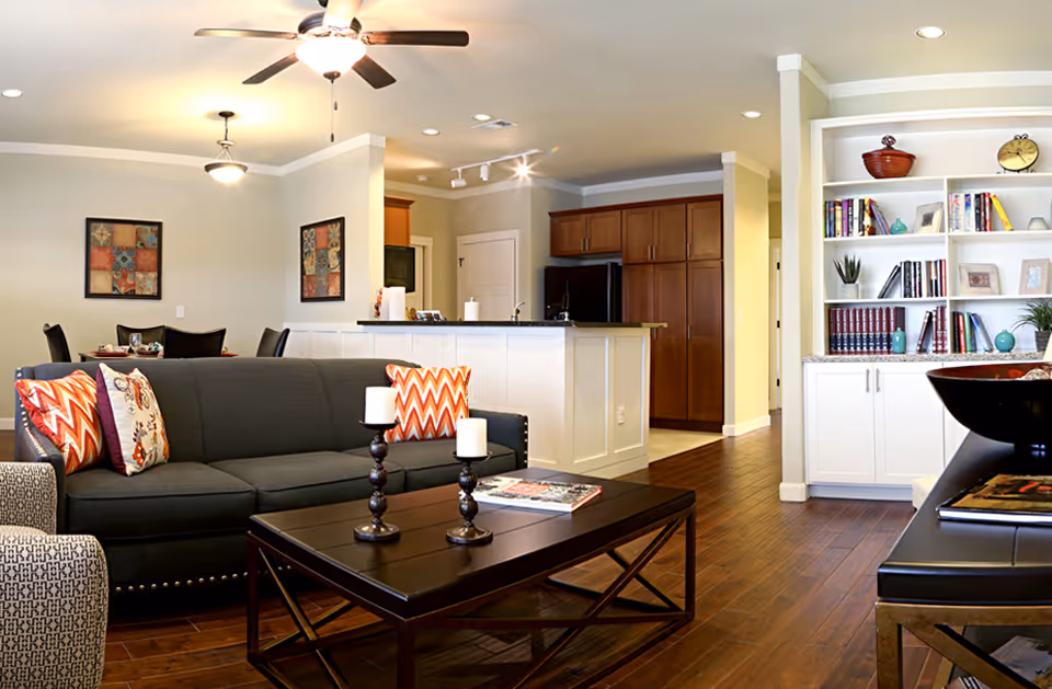 Open living area with a dark sofa and coffee table facing a built-in bookshelf, hardwood floors, and a view into the kitchen and dining area.
