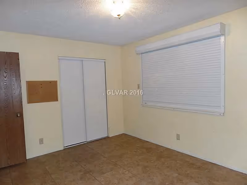 Empty room with tiled floor, sliding closet doors, a window with a closed shutter, and a wooden entry door.