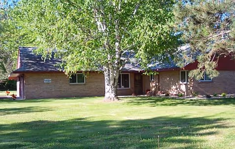 A single-story brick senior living facility exterior with green lawn and mature trees.