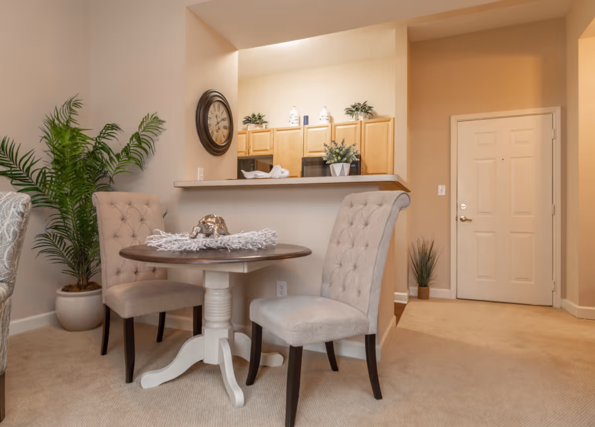 Small dining area with a round table and two upholstered chairs by a kitchen pass-through and entry door.