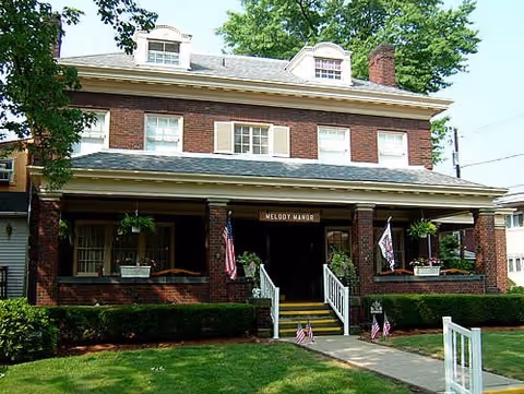 Brick two-story Melody Manor entrance with steps, flags, and hanging planters.