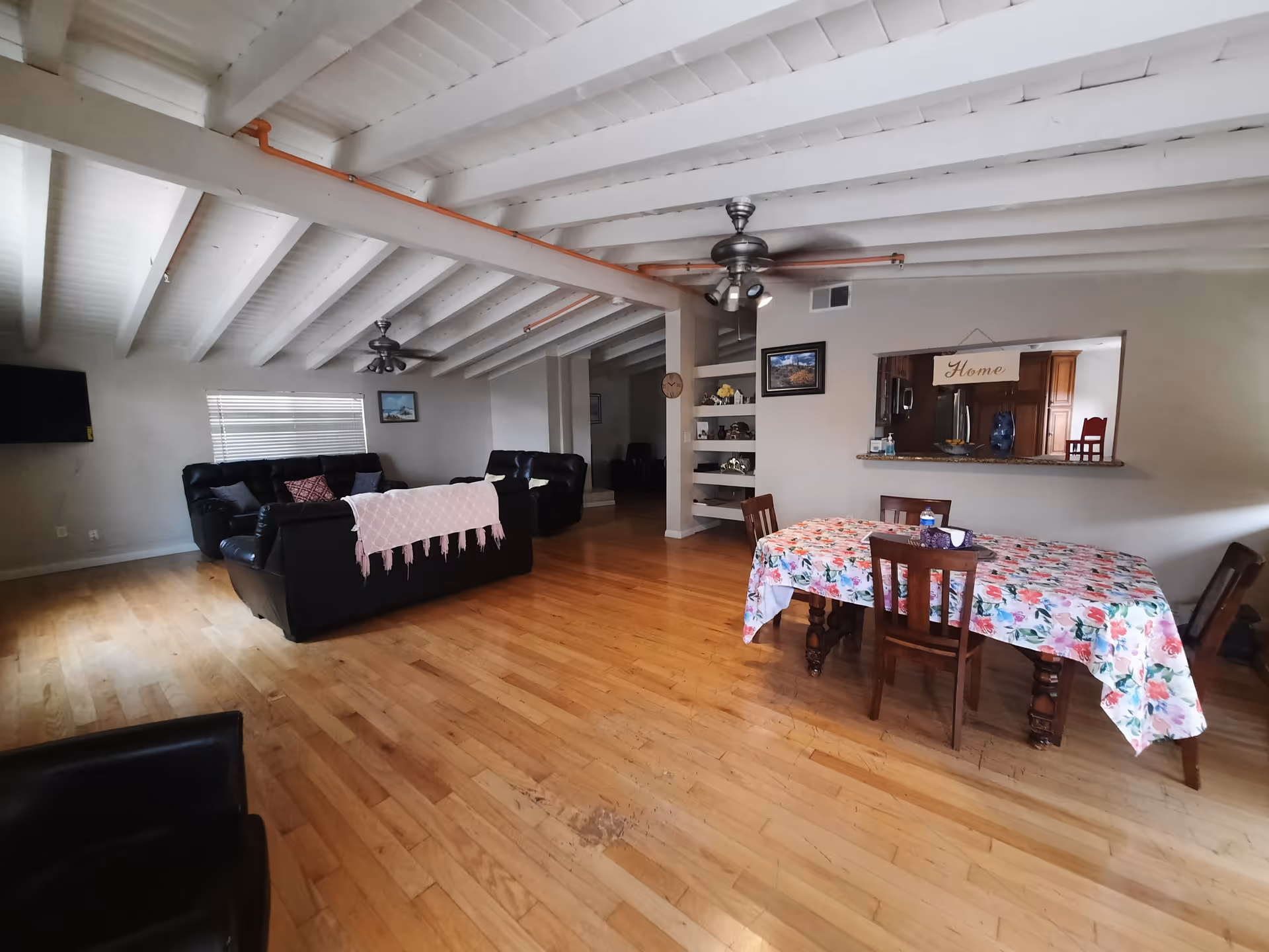 Open living and dining area with hardwood floors, leather sofas, ceiling fans, and a dining table covered with a floral tablecloth.