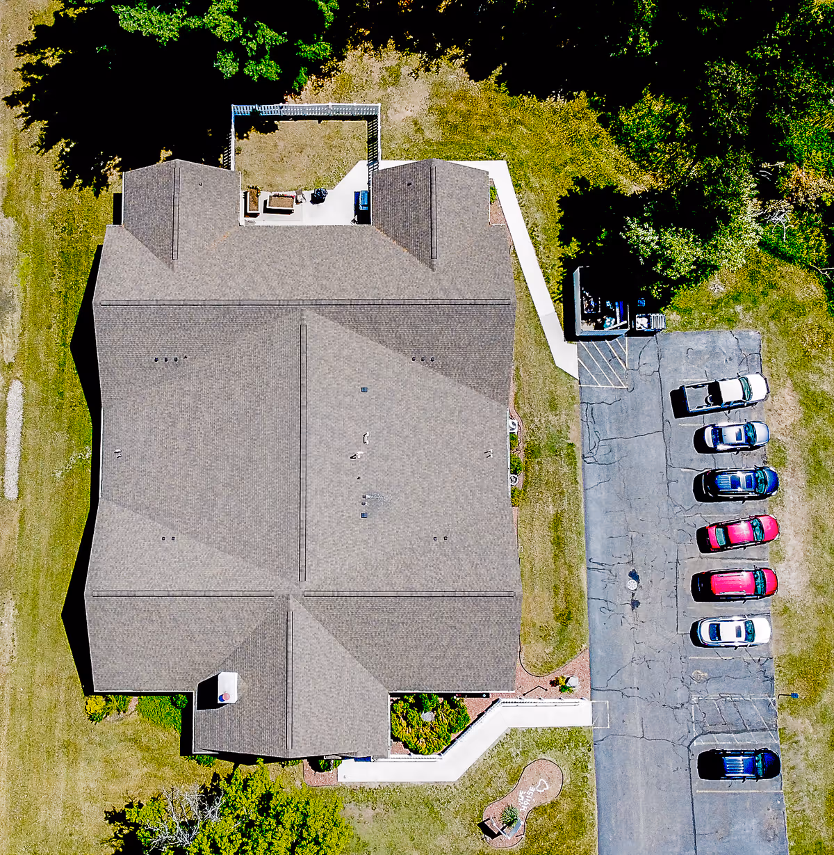 Aerial view of a senior living building showing the roof, surrounding lawn, walkways, and an adjacent parking lot with cars.