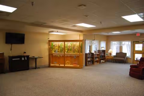 Spacious common lounge with seating, bookshelves, a display cabinet, and a wall-mounted TV.
