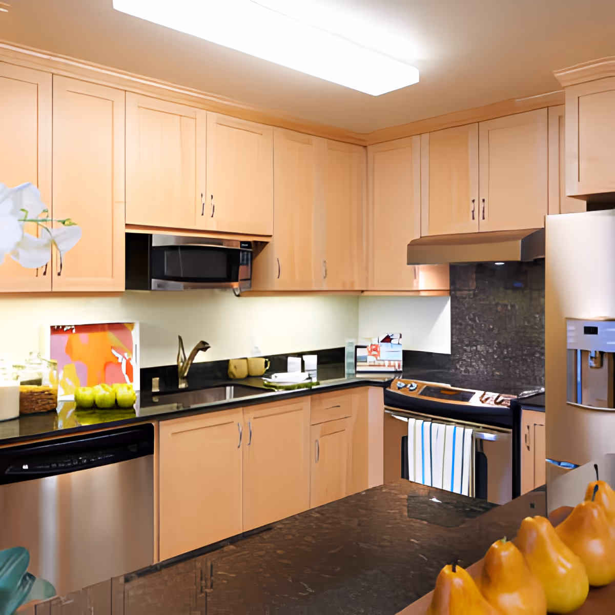 Modern kitchen with light wood cabinets, black granite countertops, stainless steel appliances, and pears on the island.