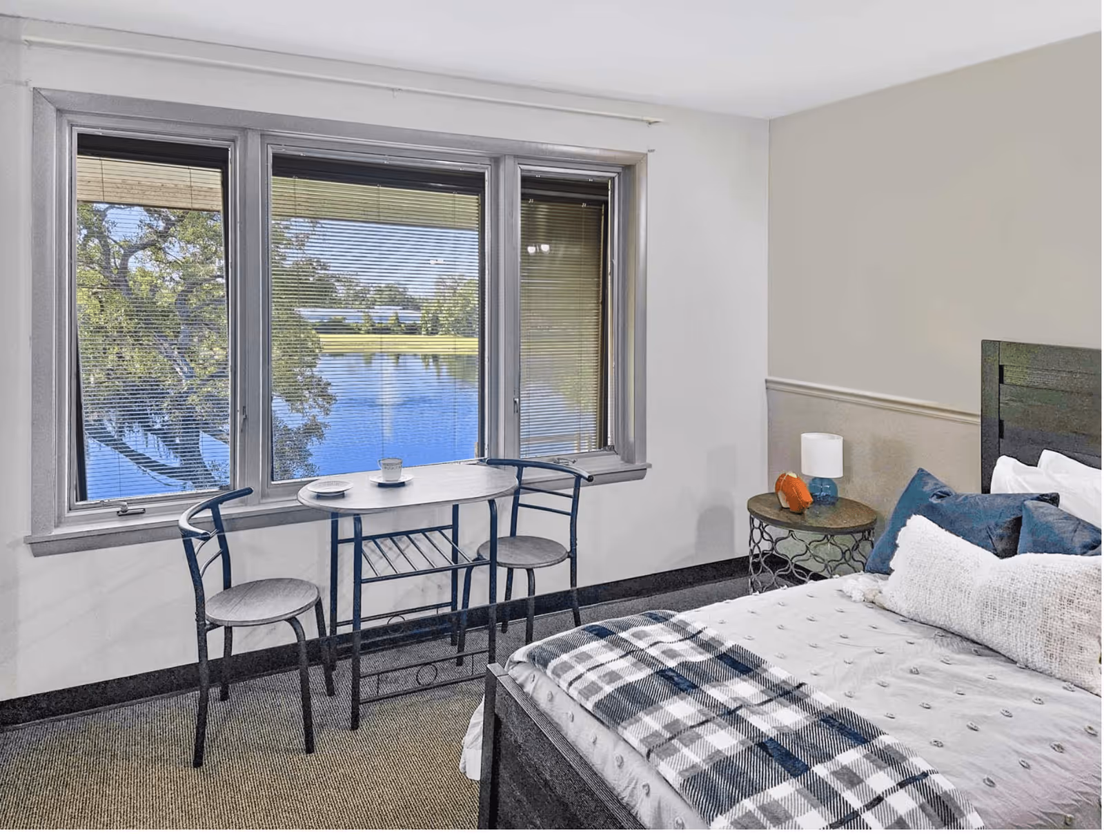 Bedroom with a bed, bedside table, and a small table with two chairs in front of a window overlooking a lake.