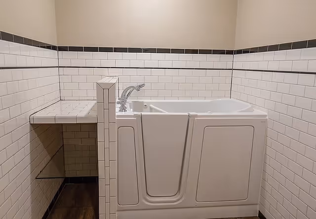 A walk-in bathtub with a side door and faucet, surrounded by white subway tile walls with a black tile border near the top, and a small tiled shelf on the left side.