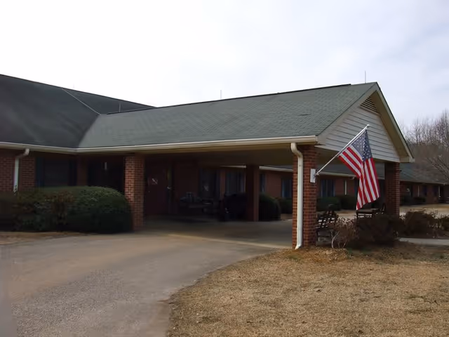 Covered brick entrance of a retirement facility with a driveway and an American flag.