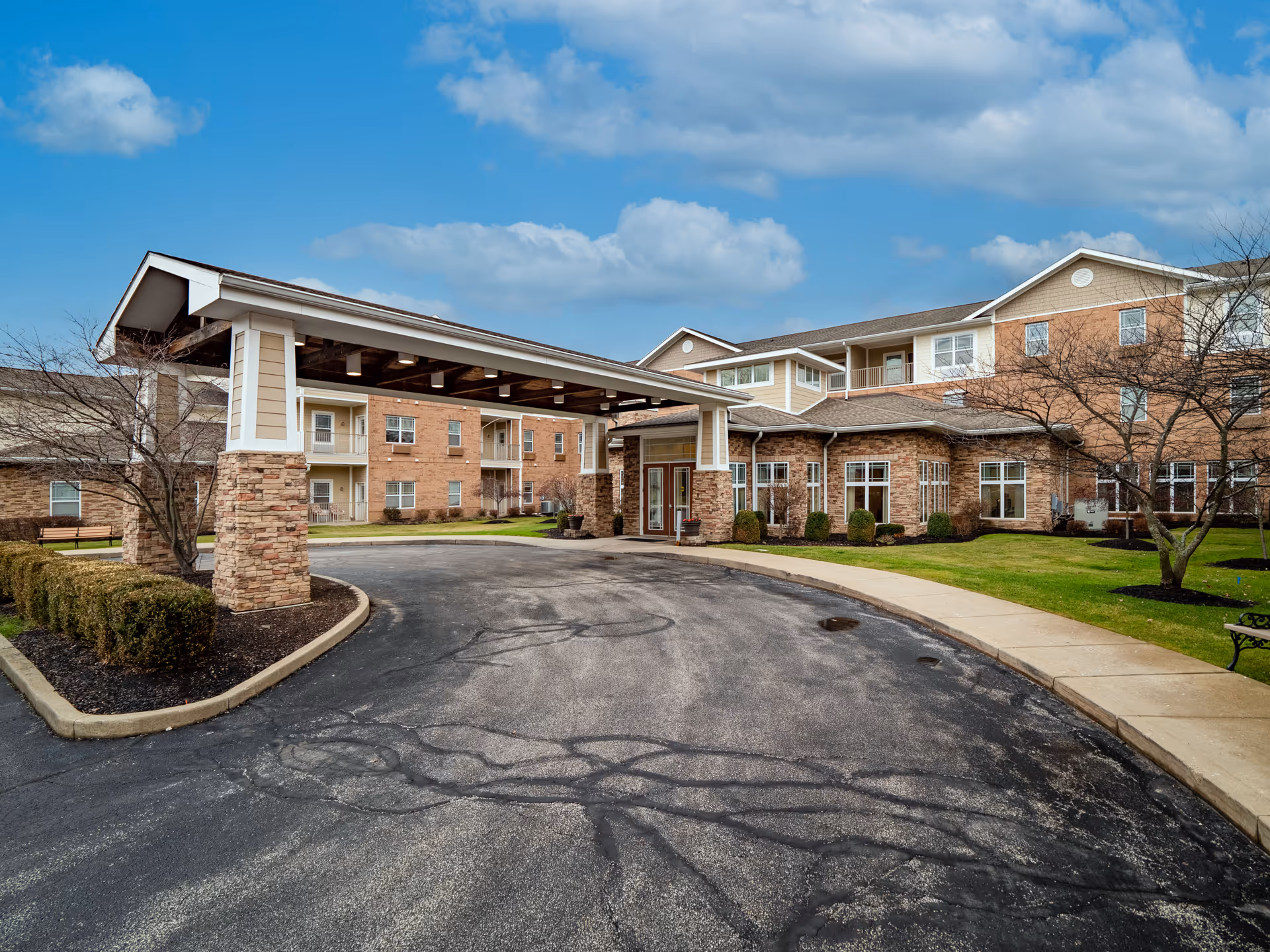 Covered entrance and driveway leading to the front of a multi-story senior living building with brick and siding exterior.